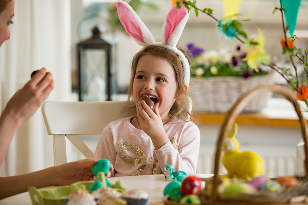 Young girl wearing bunny ears eating Easter eggs 